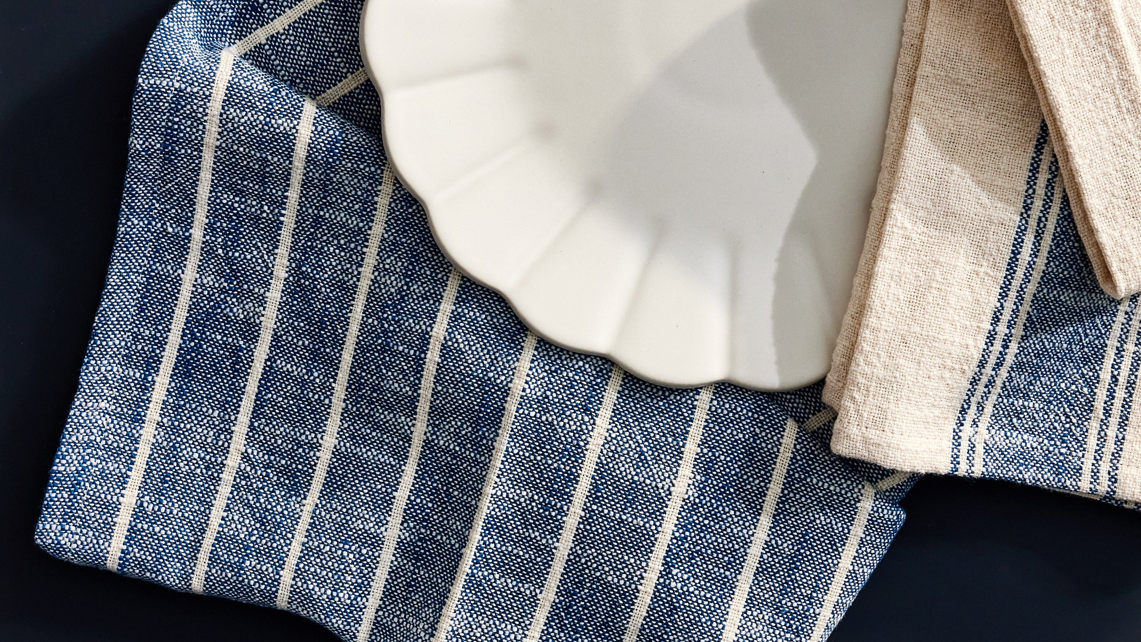 Blue and white striped towel draped over a white plate on a dark surface
